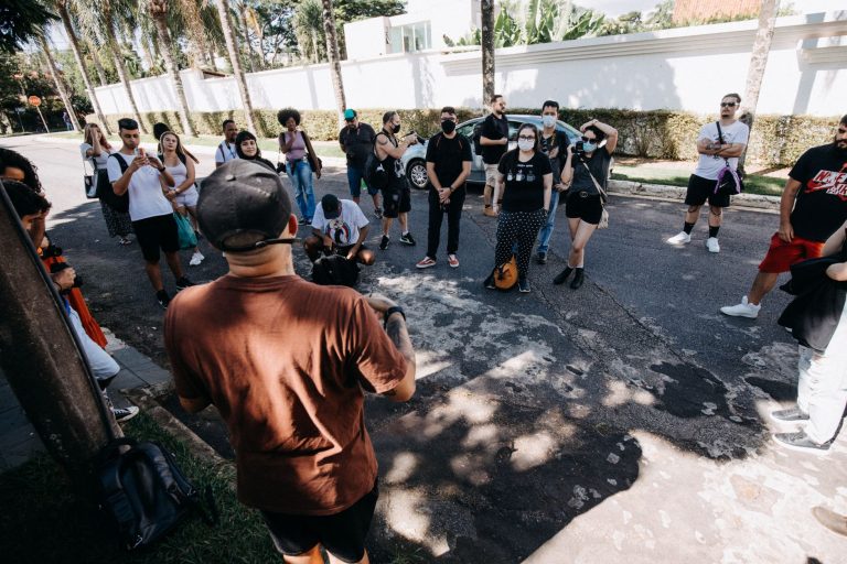 Grupo de pessoas participa de uma visita guiada em uma rua urbana durante um dia ensolarado.