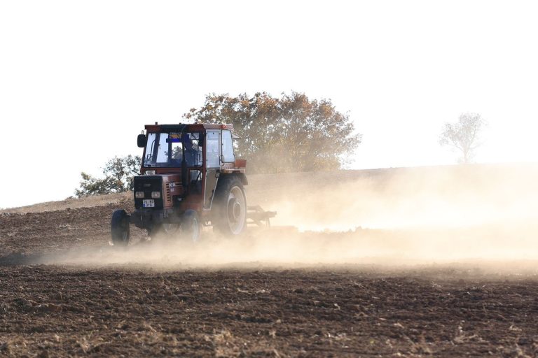 Como o financiamento organiza o início da safra agrícola 2026/27 Trator vermelho prepara o solo em um campo agrícola empoeirado.